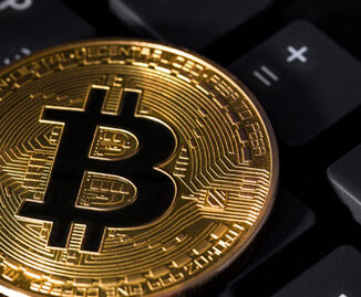 Złota moneta Bitcoin spoczywa na czarnej klawiaturze komputera, symbolizując związek między kryptowalutą a technologią cyfrową.