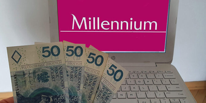 Dłoń trzyma cztery banknoty o nominale 50 zł przed białym laptopem, na ekranie którego wyświetlane jest logo banku Millennium.