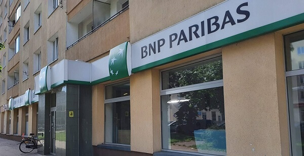 Widok z ulicy na oddział banku BNP Paribas z dużymi oknami, biało-zielonym znakiem i zaparkowanym rowerem przed budynkiem.