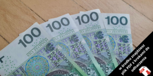 Pięć polskich banknotów o nominale 100 złotych rozłożonych na drewnianej powierzchni. Czarny ukośny baner w rogu zawiera polski tekst o pliku PDF z instrukcjami pobierania.
