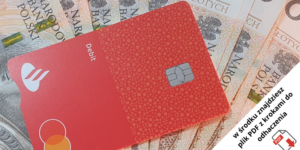 Czerwona karta debetowa leży na kilku polskich banknotach złotowych. W prawym dolnym rogu znajduje się polski komunikat o znalezieniu listy kontrolnej PDF w środku, z czerwoną ikoną PDF obok tekstu.