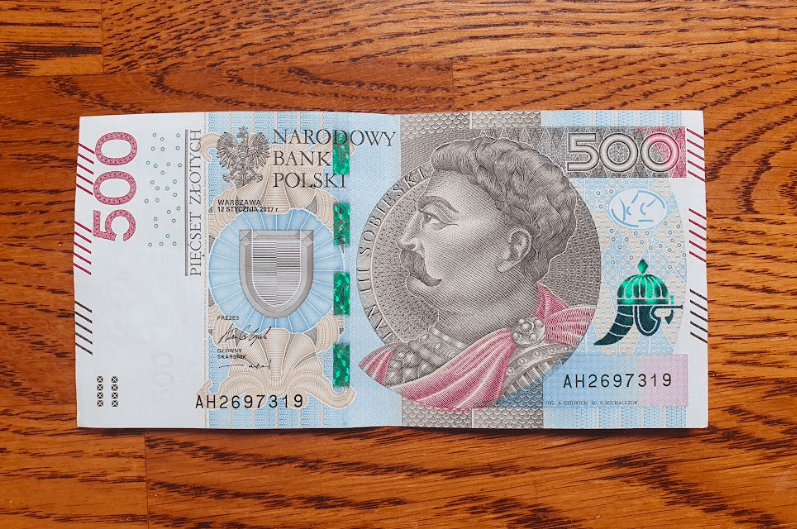 Banknot o nominale 500 zł z wizerunkiem postaci historycznej z wąsami, ozdobnymi wzorami i zabezpieczeniami, umieszczony na drewnianej powierzchni.