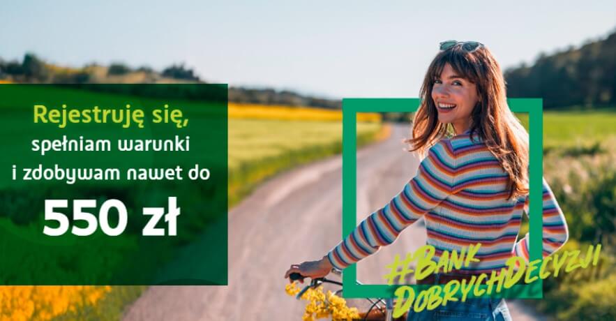 Uśmiechnięta kobieta w swetrze w paski jedzie rowerem wzdłuż wiejskiej drogi otoczonej zielonymi polami. Tekst w języku polskim oferuje do 550 zł za spełnienie warunków rejestracji. Na obrazie pojawiają się hasztagi i grafiki promocyjne.
