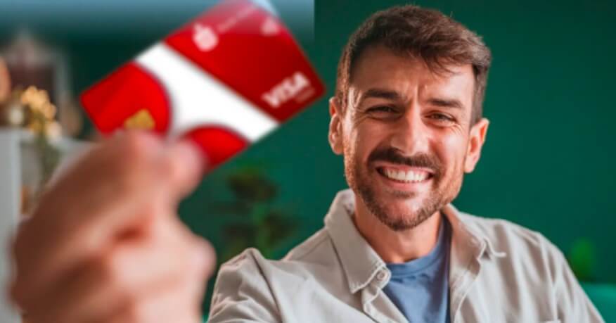 Uśmiechnięty mężczyzna trzyma czerwoną kartę kredytową VISA w kierunku kamery, przy czym karta jest lekko nieostra. Tło jest zielone i delikatnie rozmyte.